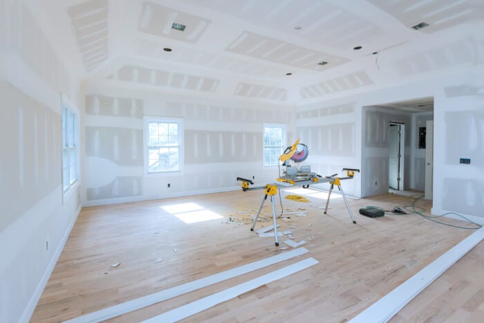 A room under construction with unfinished drywall installation, wood flooring, and a miter saw on a stand; white trim boards and sawdust scattered on the floor—an example of Knoxville home improvement in progress.