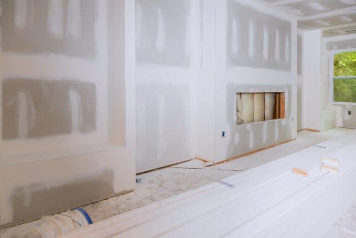 Room under construction featuring unfinished drywall installation, exposed insulation in one section of the wall, and stacks of white baseboards or trim on the floor—a great opportunity for home remodeling and professional painting.