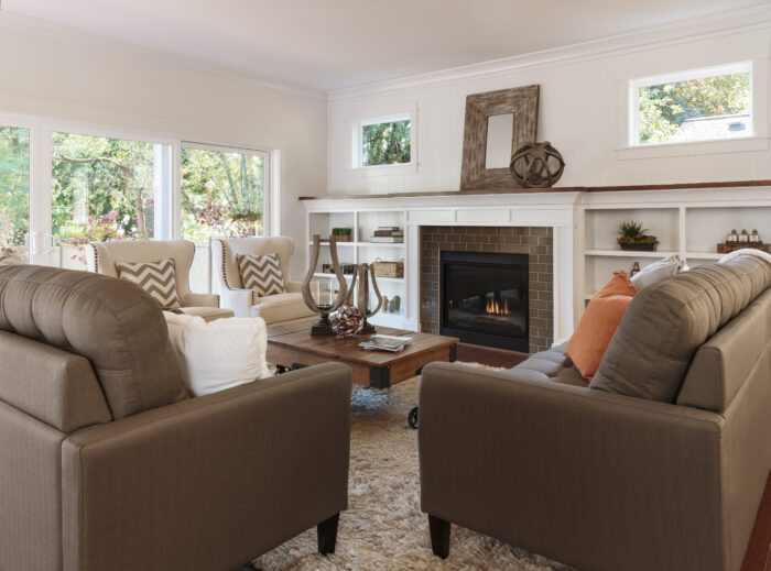 A modern living room features two brown sofas, two armchairs, a wooden coffee table, a fireplace, and large windows bathing the space in natural light—showcasing Knoxville home improvement and quality craftsmanship.